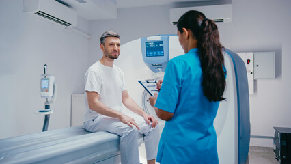 Patient pointing at form while speaking with nurse in turquoise scrubs holding clipboard....