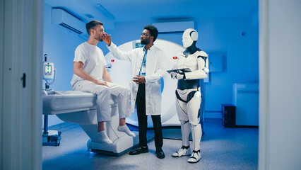 Caucasian male holding lower back and speaking to attentive doctor with beard and glasses during examination. Robotic assistant recording diagnostic input using digital tablet device.