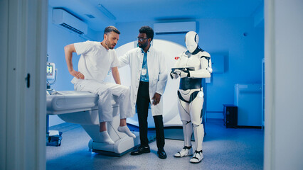 Worried Caucasian male holding head while getting examined by attentive physician checking symptoms. Humanoid robot processing data on tablet and monitoring situation in clinical environment.