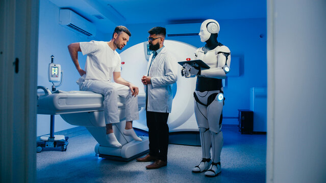 Exhausted man sitting on hospital bed rubbing forehead while describing headache to doctor in lab coat. Robotic assistant processing clinical data and noting symptoms on digital device during session.