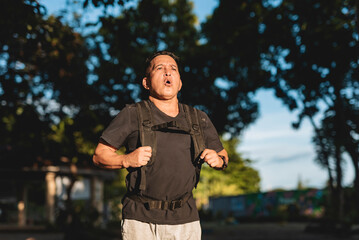 Middle aged Southeast Asian man runs through park wearing weighted backpack, regulating his breathing during an intense rucking workout. VO2 max run.
