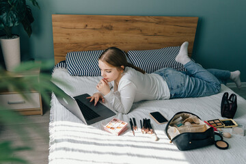 Teenage girl watching makeup tutorial on laptop while lying on bed