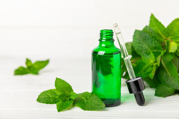 Essential oil mint on a wooden background. Peppermint essential oil with fresh mint leaves. A bottle of aromatherapy oil. Mint extract. The concept of natural cosmetics, spa care. copy space