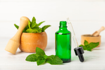 Essential oil mint on a wooden background. Peppermint essential oil with fresh mint leaves. A bottle of aromatherapy oil. Mint extract. The concept of natural cosmetics, spa care. copy space