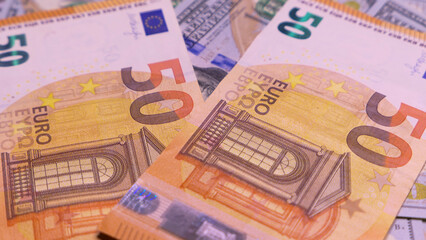 Two brightly colored 50 euro banknotes on a pile of various currency bills, emphasizing wealth and economic exchange. Text includes 