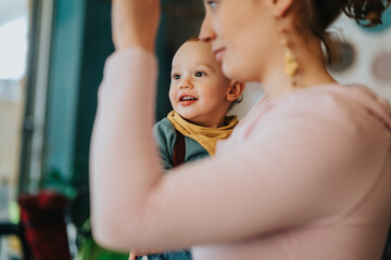 A smiling toddler dressed warmly is held by an adult. The atmosphere is joyful and relaxed with...