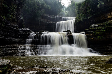 Fototapeta premium Wei sawdong , a multitiered waterfall cascading down rocky cliffs, surrounded by lush green foliage. A beautiful waterfall in Meghalaya.