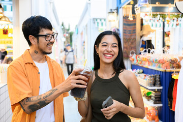 Happy couple sharing cold drink while walking in street market in Bangkok