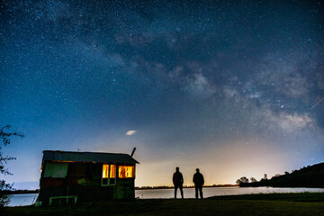 A tranquil night at Lake Kerkini, where a wooden cabin glows warmly under a breathtaking Milky Way, Greece