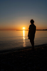 Fototapeta premium silhouette of a girl or woman standing on the beach of lake constance and watching the sunset over the island of lindau