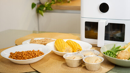 Air fryer cooking various dishes including corn, muffins, and vegetables