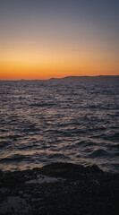 Rocky coastline meeting calm ocean under a vibrant sunset sky
