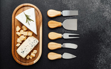 A selection of cheeses on a wooden tray accompanied by various cheese knives