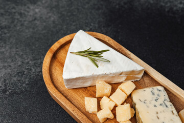 Selection of gourmet cheeses on a wooden platter with fresh herbs in a dim light