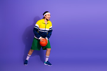 Young male athlete in retro activewear standing with a basketball against a vibrant purple background showcasing sports style.