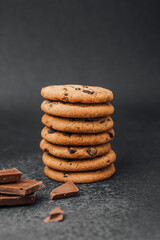 Freshly baked chocolate chip cookies stacked with chocolate pieces nearby