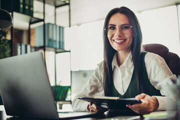 Plakat Confident businesswoman working in a modern office environment, holding documents, showcasing professionalism and success