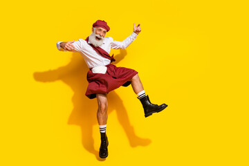 Fototapeta na wymiar Energetic elderly man in traditional Scottish attire jumping against a vibrant yellow background expressing joy and fun