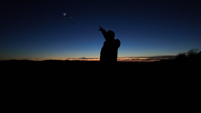 Silhouette of a man observing Milky Way stars, planets and other celestial objects from a dark countryside location.