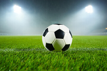 Fototapeta premium Soccer ball on grass field at night illuminated by stadium lights photo