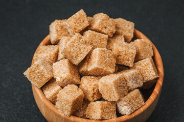 Brown sugar cubes arranged in a wooden bowl on a dark surface