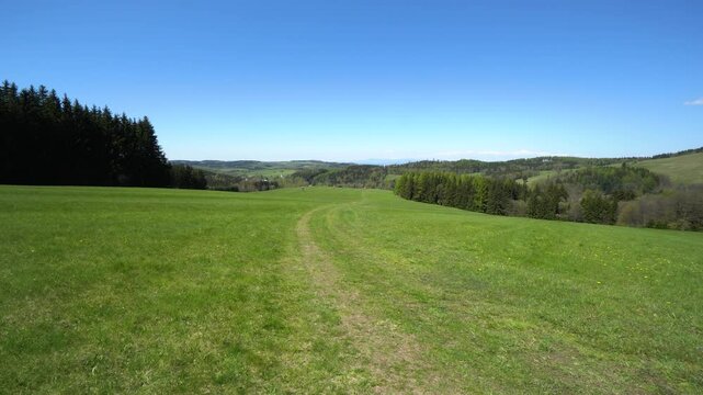 A hilly rural area on a sunny day - view from a trodden track in a meadow