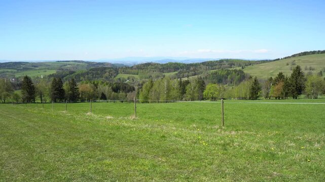 An electric rope fence stretched across a green meadow in a vast valley on a sunny day