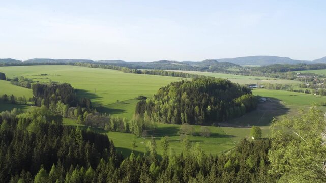 A vast green valley with thick patches of woods on a sunny day - top view
