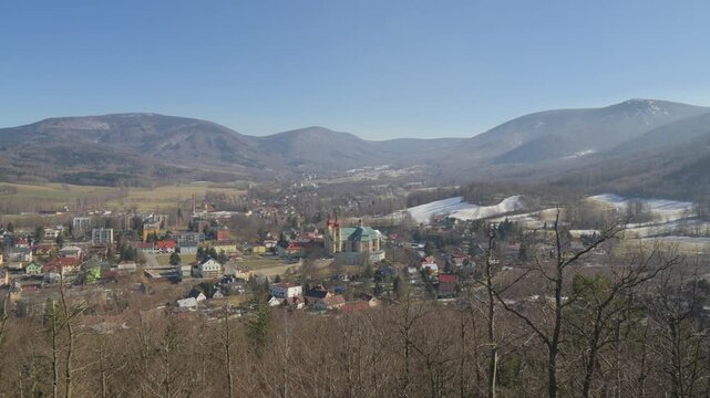 A quaint European town surrounded by hills and woods with bare trees on a winter day - top view