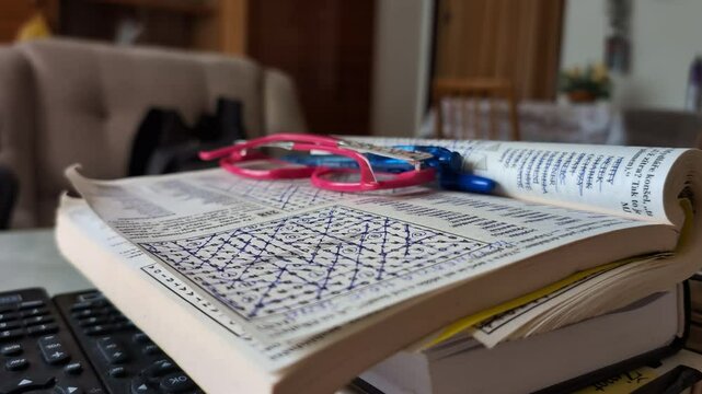A book with a finished crossword puzzle on a page on a table - glasses between the pages - closeup