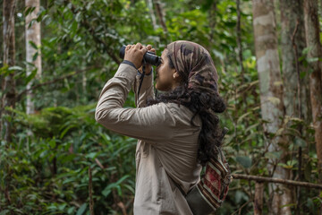 Female explorer birdwatching in the Amazon rainforest, using a binoculars