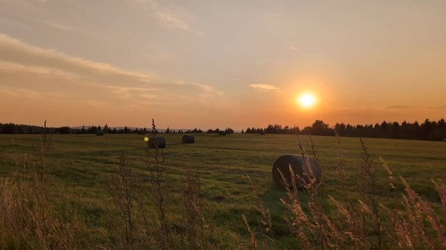 Sun sets over a rural field with hay bales in a countryside