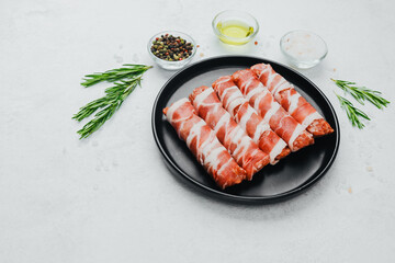 Bacon wrapped sausages on black plate with spices and rosemary