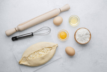 Raw khachapuri with egg yolk and cheese on white background with ingredients