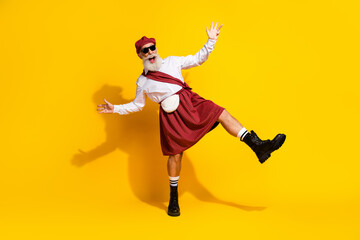 Elderly man dressed in a traditional Scottish outfit posing cheerfully against a vibrant yellow background