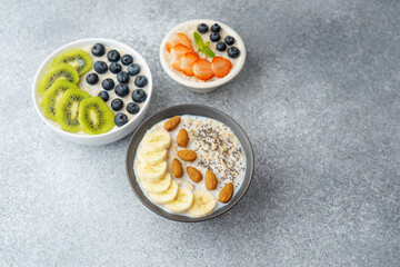 Variety of oatmeal bowls with fruits nuts and chia seeds on gray table