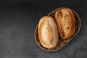 Freshly baked loaves of bread in a woven basket on a dark surface