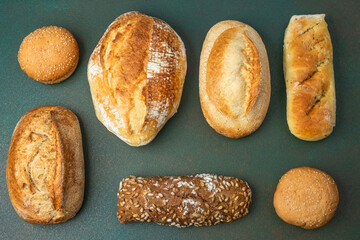 Different types of bread displayed on a green surface in a bakery setting