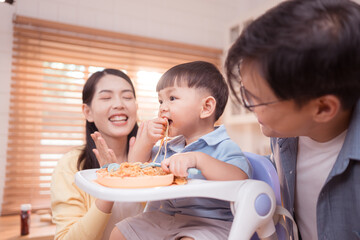 Happy Asian parents enjoying mealtime with their toddler in the kitchen