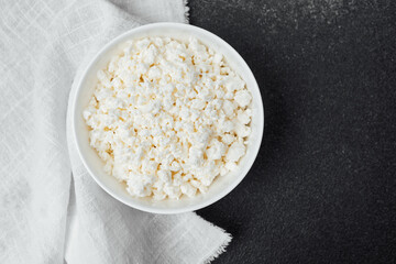 Bowl of fresh cottage cheese on a dark surface with a cloth