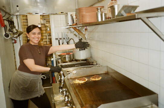 Portrait of smiling woman gesturing while posing near griddle in restaurant kitchen
