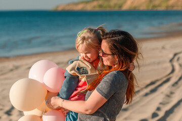 A young mother with her daughter little child with balloons by the sea with a beautiful landscape