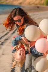 A young mother with her daughter little child with balloons by the sea with a beautiful landscape