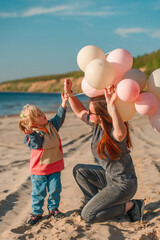 A young mother with her daughter little child with balloons by the sea with a beautiful landscape