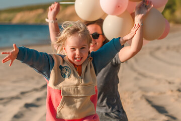 A young mother with her daughter little child with balloons by the sea with a beautiful landscape