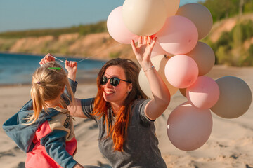 A young mother with her daughter little child with balloons by the sea with a beautiful landscape