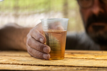 Hands of lonely drunk man with dirty nails and raised cuticles, holding glass of whiskey on blurred background
