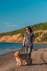 A curly-haired brown Labradoodle or Cavapoo dog with a young woman are best friends by the sea at sunset.