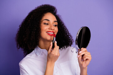 Young woman applying red lipstick while looking in a mirror, showing elegance and confidence...