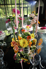 Vibrant floral arrangement with assorted flowers, candles, and colorful citrus fruits on a mirrored table. Bright and elegant decor perfect for events or special occasions.